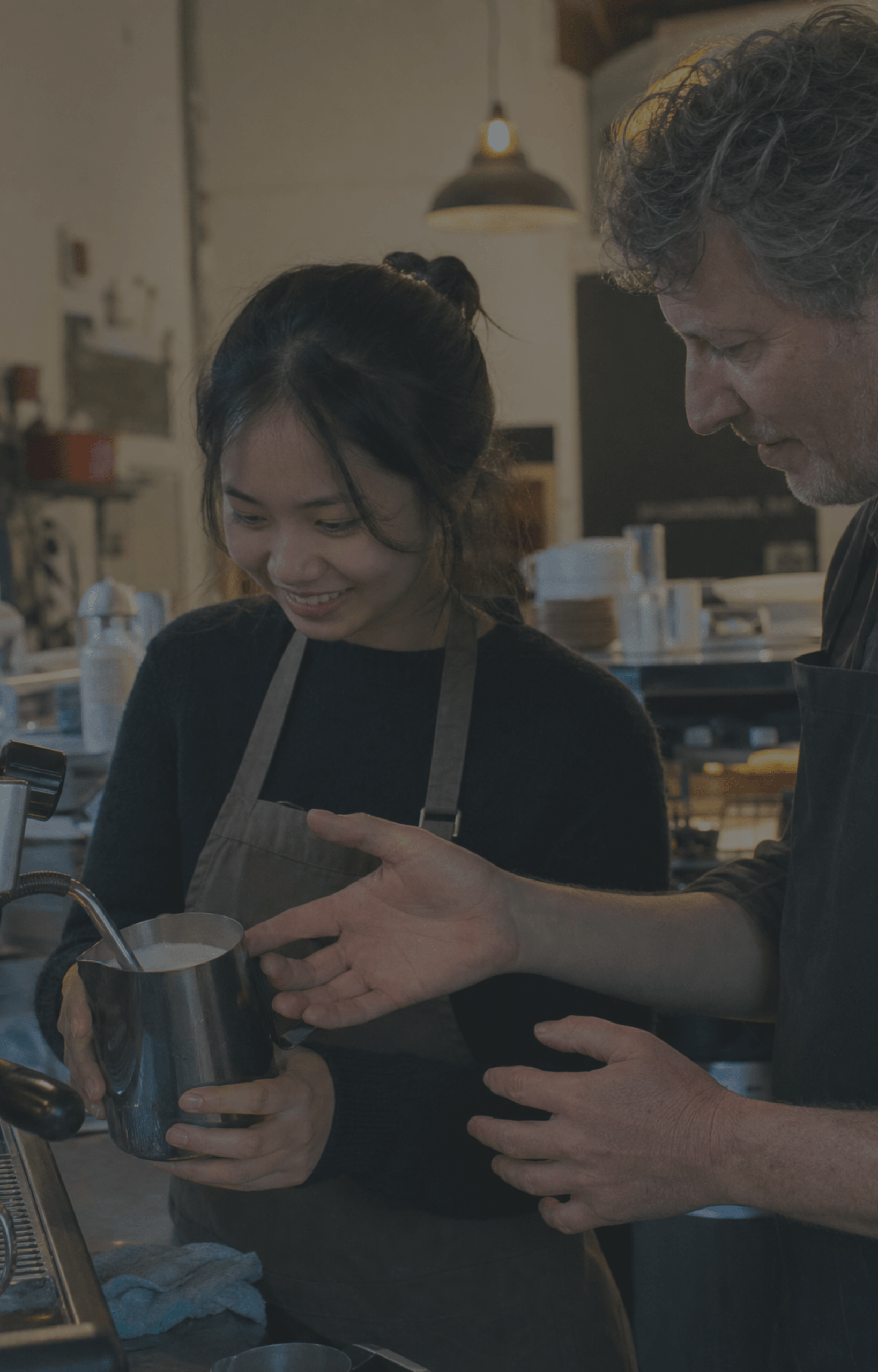 east-asian-woman-barista-milk-steaming-pakeha-trainer-cafe-dark-overlay-nz